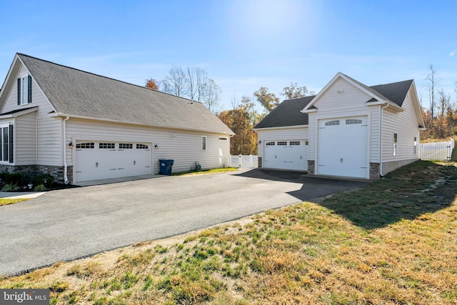 view of side of home featuring a lawn, stone siding, a detached garage, an outbuilding, and fence