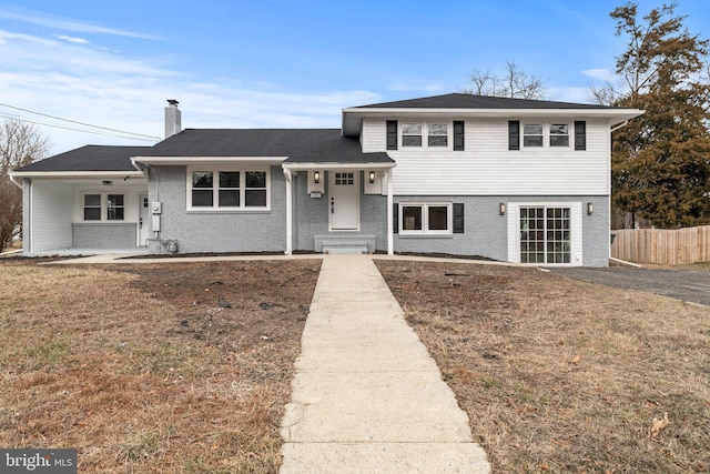 tri-level home featuring a chimney, fence, and brick siding