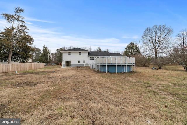 rear view of property featuring fence, an outdoor pool, and a yard