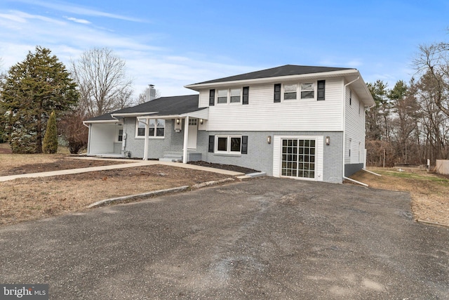 tri-level home featuring brick siding, driveway, and a chimney