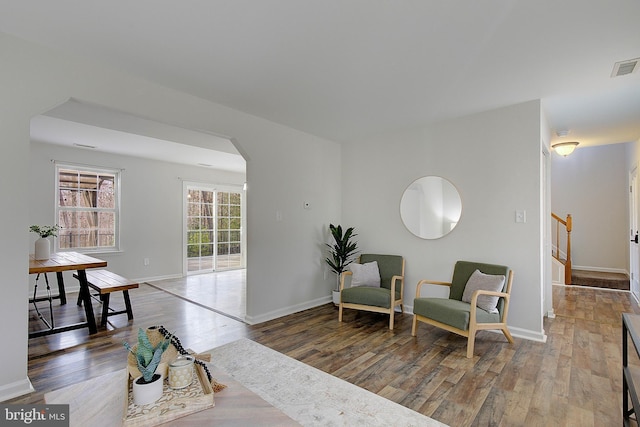 living area with arched walkways, visible vents, wood finished floors, baseboards, and stairs