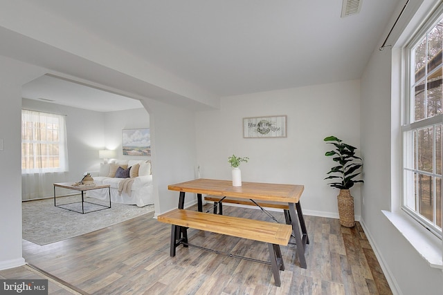 dining space featuring arched walkways, wood finished floors, visible vents, and baseboards