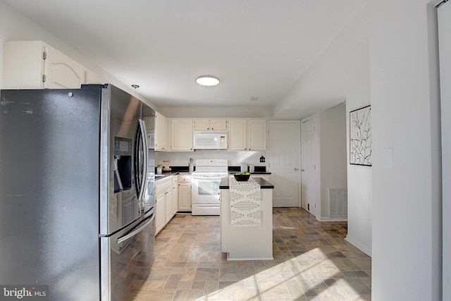 kitchen with visible vents, stone finish floor, white cabinetry, a kitchen island, and white appliances