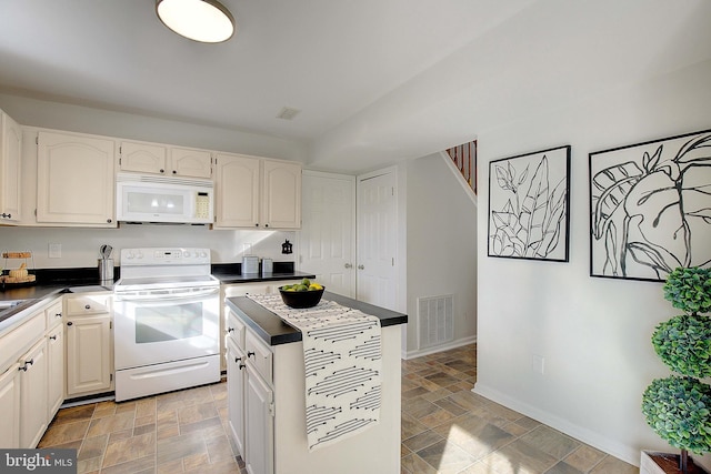 kitchen with dark countertops, visible vents, stone finish floor, white appliances, and baseboards