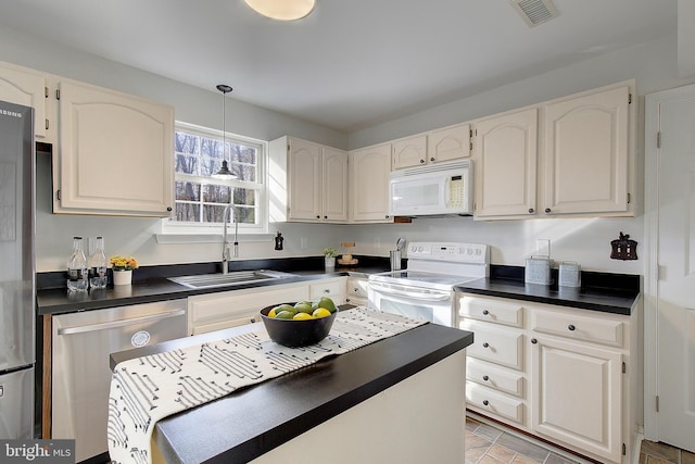 kitchen with dark countertops, white appliances, visible vents, and a sink