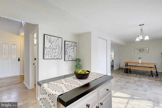 kitchen with a notable chandelier, hanging light fixtures, stone finish floor, white cabinets, and baseboards