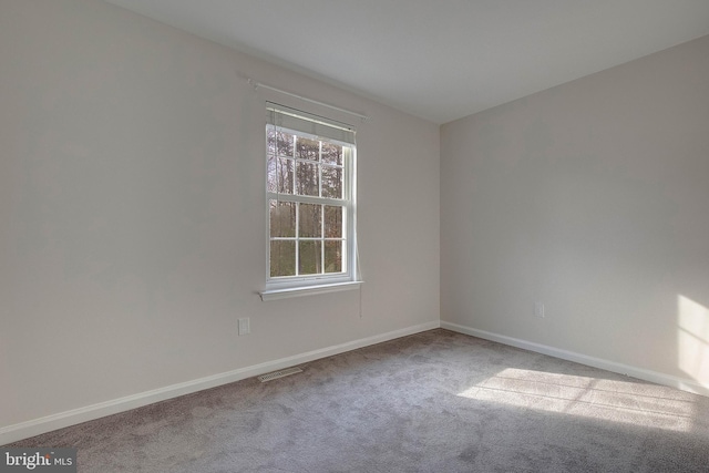 spare room with carpet floors, visible vents, and baseboards