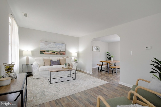 living room featuring visible vents, baseboards, arched walkways, and wood finished floors