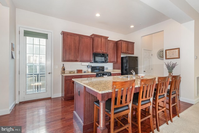 kitchen with baseboards, recessed lighting, wood finished floors, black appliances, and a kitchen island with sink