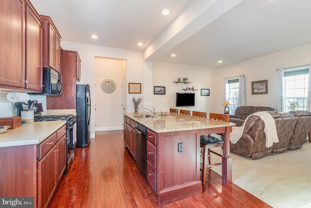 kitchen with open floor plan, a breakfast bar area, dark wood-style floors, black appliances, and a sink