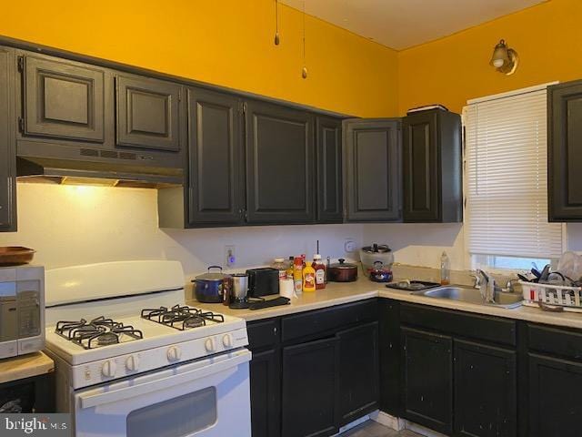 kitchen with white gas range oven, stainless steel microwave, light countertops, under cabinet range hood, and a sink