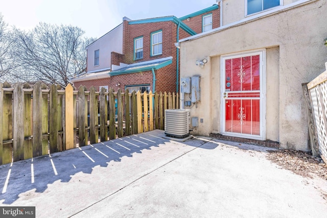 view of exterior entry with stucco siding, fence, brick siding, and central air condition unit