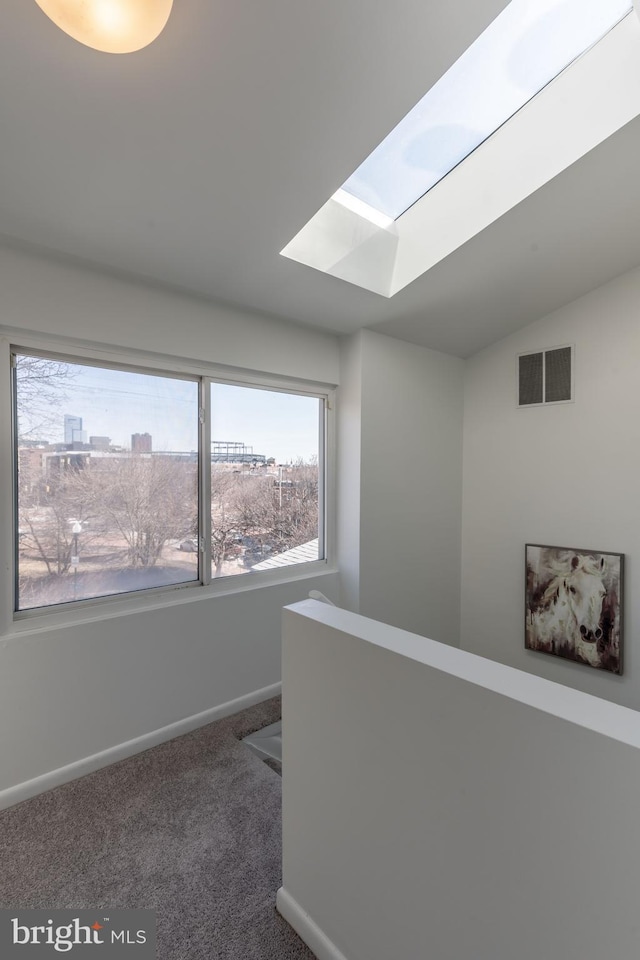 hallway with visible vents, baseboards, lofted ceiling with skylight, carpet, and an upstairs landing