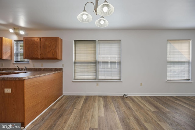kitchen featuring dark countertops, wood finished floors, brown cabinetry, a chandelier, and baseboards