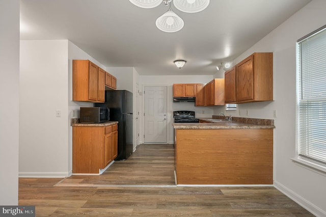 kitchen with black range with electric stovetop, under cabinet range hood, a sink, and brown cabinets