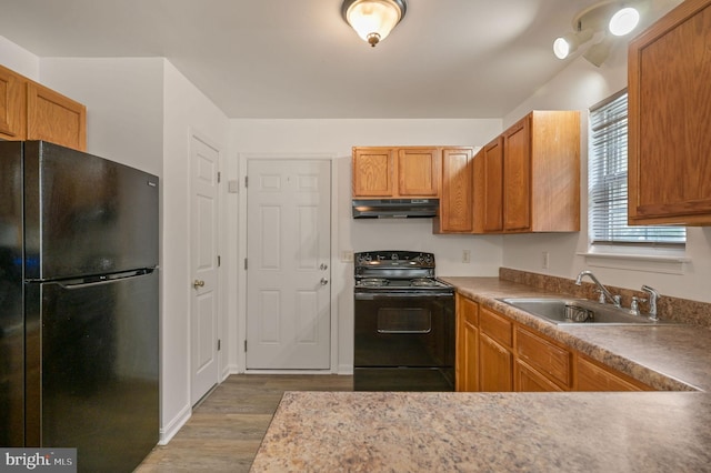 kitchen featuring black appliances, under cabinet range hood, a sink, wood finished floors, and brown cabinetry