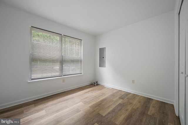 spare room featuring electric panel, wood finished floors, and baseboards