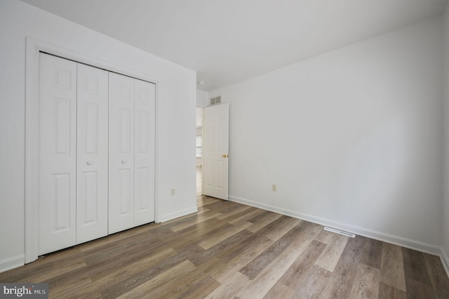 unfurnished bedroom with wood finished floors, baseboards, and a closet