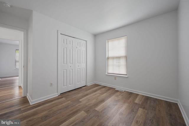unfurnished bedroom with wood finished floors, baseboards, and a closet