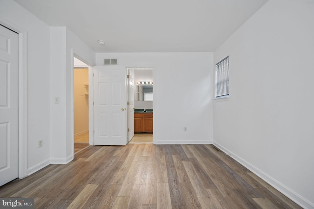 unfurnished bedroom with wood finished floors, baseboards, and ensuite bath