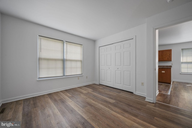 unfurnished bedroom with dark wood-style flooring, a closet, and baseboards