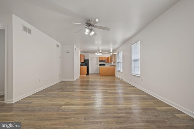 unfurnished living room featuring a ceiling fan, dark wood finished floors, baseboards, and a chandelier