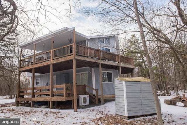 snow covered back of property with ac unit, a wooden deck, an outbuilding, and a storage shed