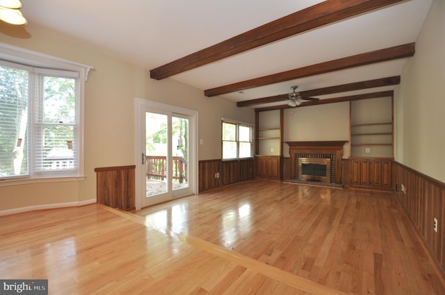 unfurnished living room with a healthy amount of sunlight, a wainscoted wall, light wood-type flooring, and a fireplace