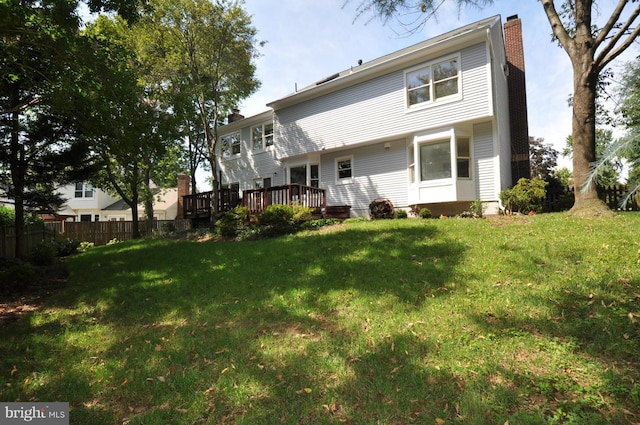 back of house featuring a chimney, fence, a deck, and a yard