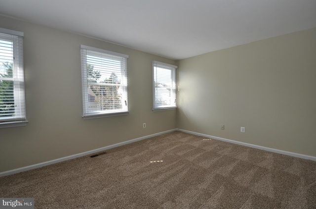 empty room featuring carpet floors, visible vents, and baseboards