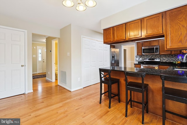 kitchen with light wood-style flooring, stainless steel appliances, a sink, visible vents, and tasteful backsplash