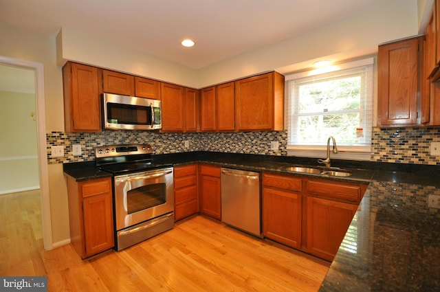 kitchen with light wood-style flooring, a sink, appliances with stainless steel finishes, backsplash, and dark stone countertops