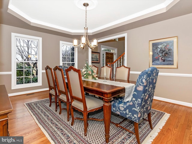 dining area with light wood-style floors, a tray ceiling, baseboards, and an inviting chandelier