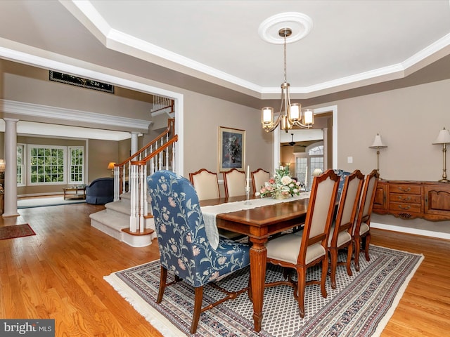 dining area with a tray ceiling, wood finished floors, ornate columns, and an inviting chandelier