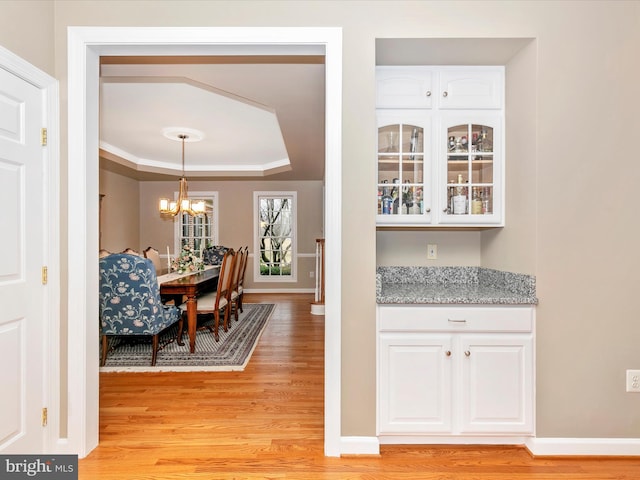 dining area featuring a chandelier, a raised ceiling, light wood-style flooring, and baseboards