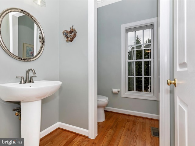 half bath with visible vents, baseboards, toilet, wood finished floors, and a sink