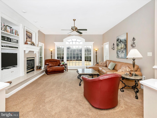 living room featuring built in shelves, carpet, a glass covered fireplace, and a ceiling fan