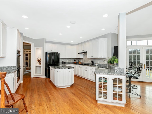 kitchen with light wood-style floors, dark stone countertops, under cabinet range hood, black appliances, and white cabinetry