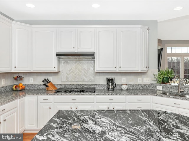 kitchen with gas cooktop, under cabinet range hood, a sink, white cabinets, and dark stone countertops