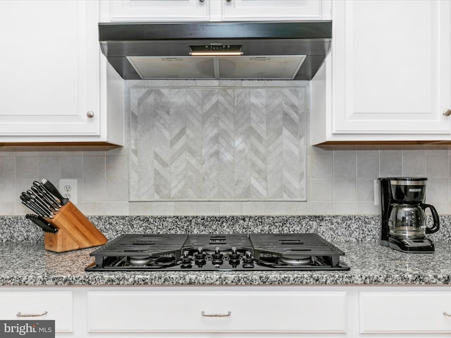 kitchen featuring black gas stovetop, stone countertops, under cabinet range hood, white cabinets, and backsplash