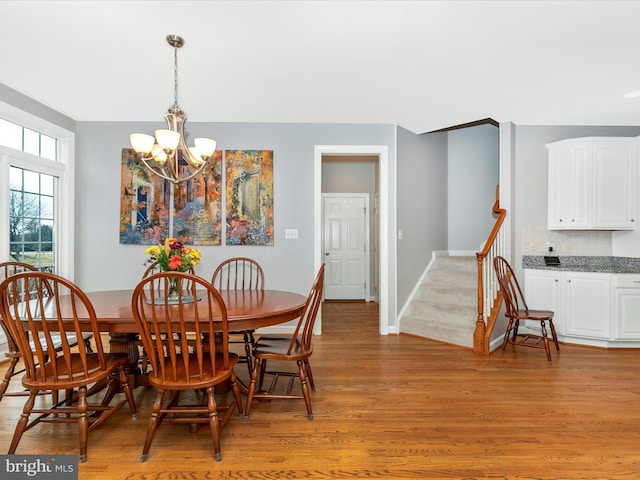 dining room with baseboards, stairway, light wood-type flooring, and a notable chandelier