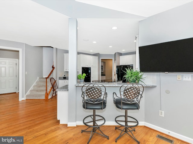 kitchen with visible vents, light wood finished floors, black appliances, and white cabinetry