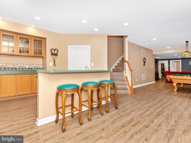 kitchen with light wood-style flooring, recessed lighting, pool table, a kitchen breakfast bar, and glass insert cabinets