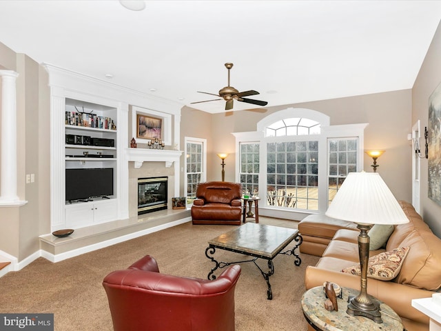 carpeted living area with ornate columns, built in shelves, a large fireplace, and a ceiling fan