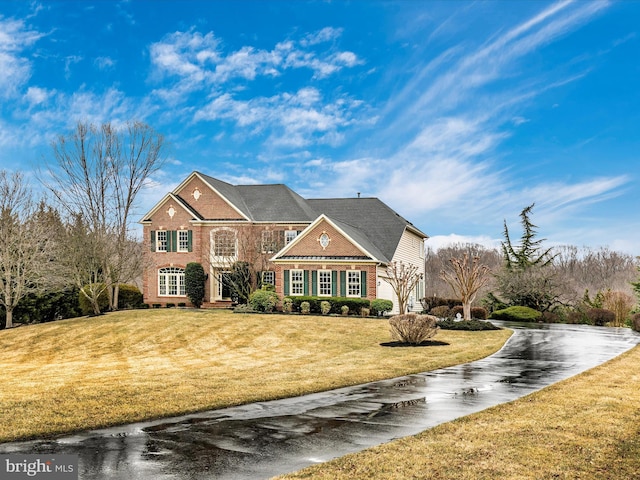 colonial inspired home with a garage, a front yard, brick siding, and driveway