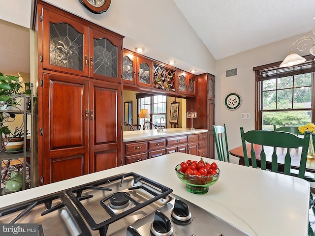 kitchen with visible vents, vaulted ceiling, glass insert cabinets, and light countertops