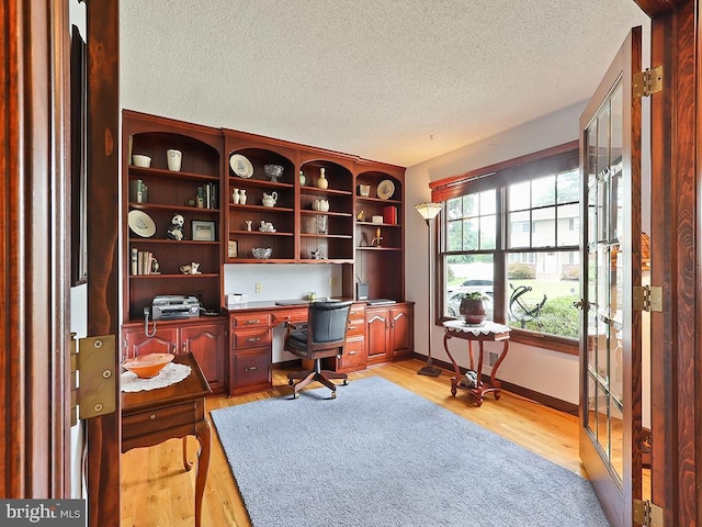 home office featuring a textured ceiling, light wood finished floors, and baseboards