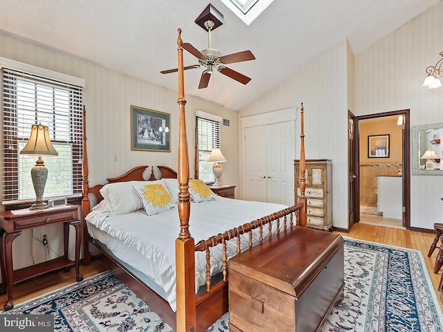 bedroom with light wood finished floors, a closet, lofted ceiling with skylight, a ceiling fan, and connected bathroom