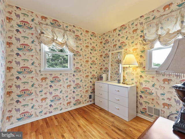 interior space featuring baseboards, light wood finished floors, visible vents, and wallpapered walls