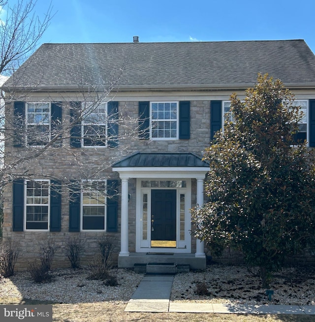 view of front of house with stone siding, a shingled roof, a standing seam roof, and metal roof